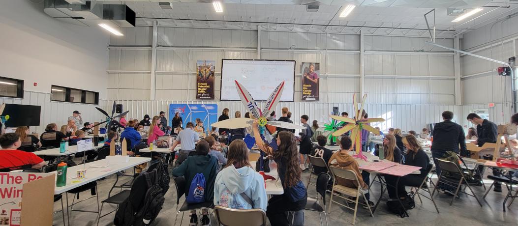 All teams listening to presenter with wind turbines on table.